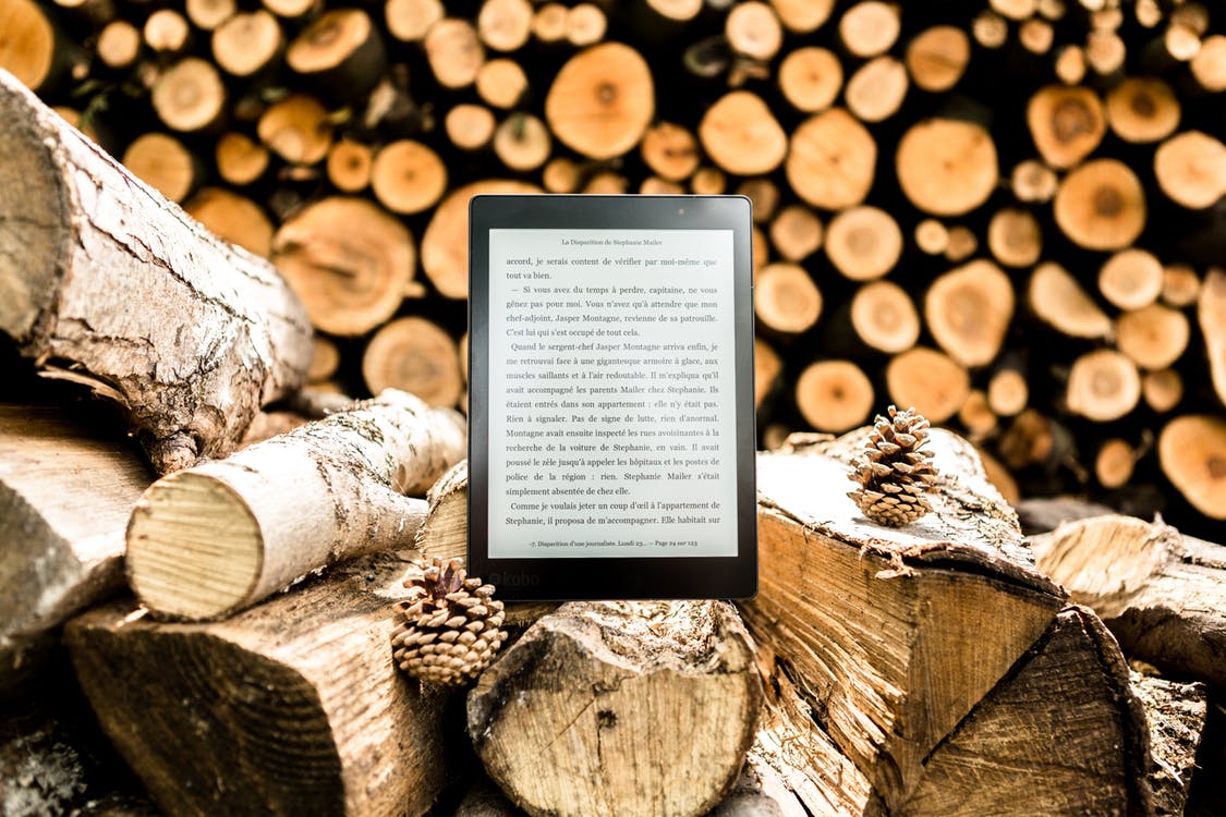 Black E-book Reader on Brown Tree Logs
