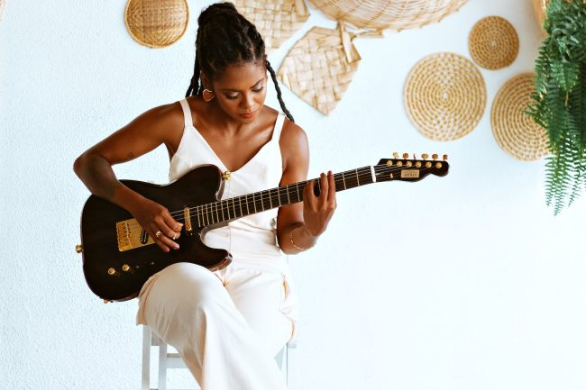 photo of a young woman sitting and playing an electric guitar