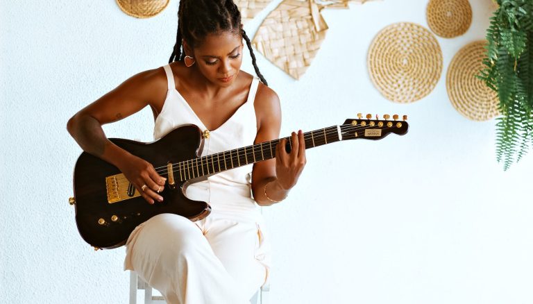 photo of a young woman sitting and playing an electric guitar