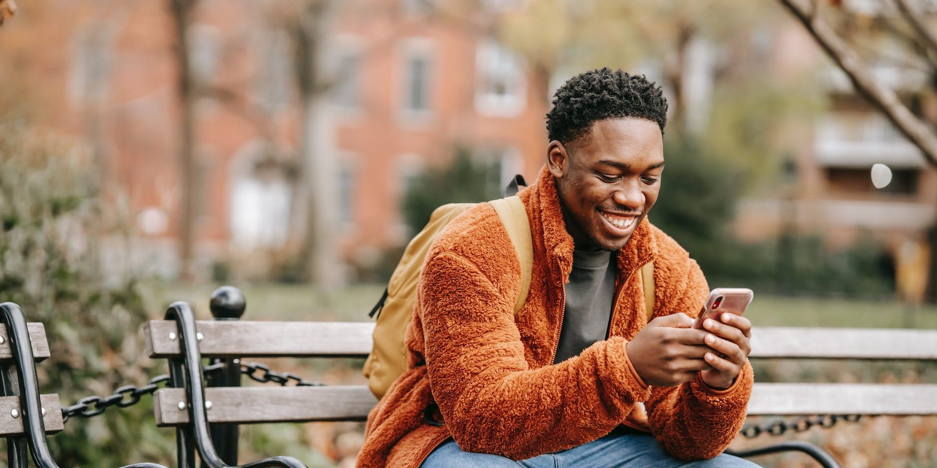 delightful african american man surfing modern cellphone in city park