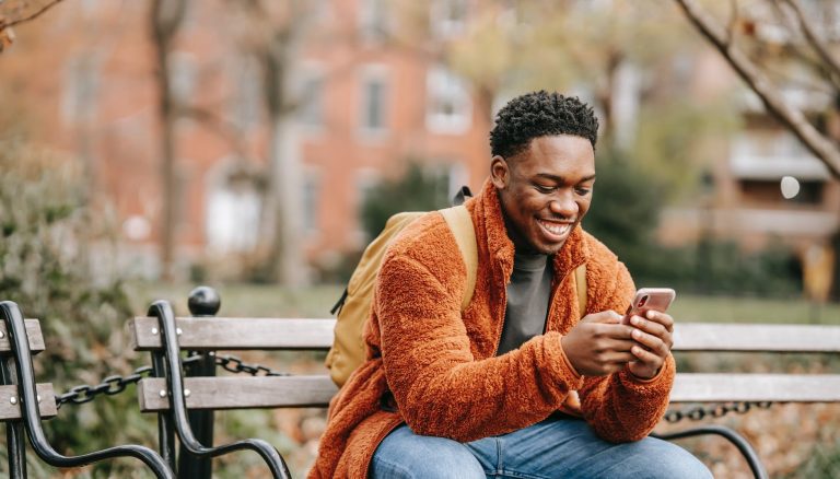 delightful african american man surfing modern cellphone in city park