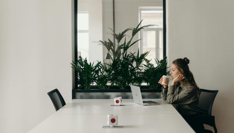 woman in black and gray jacket sitting on chair in front of silver macbook
