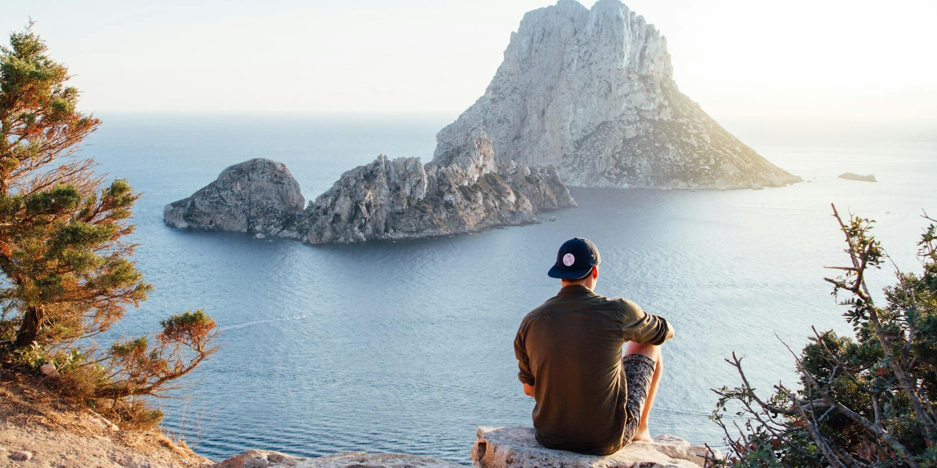 rear view of man sitting on rock by sea