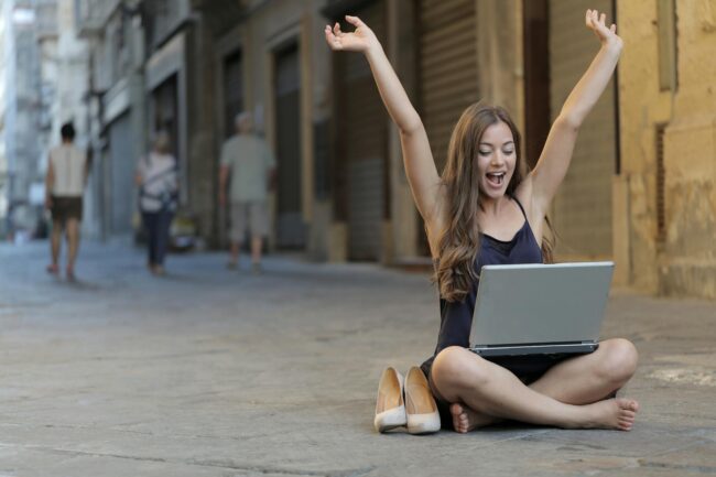 woman raising her hands up while sitting on floor with macbook pro on lap
