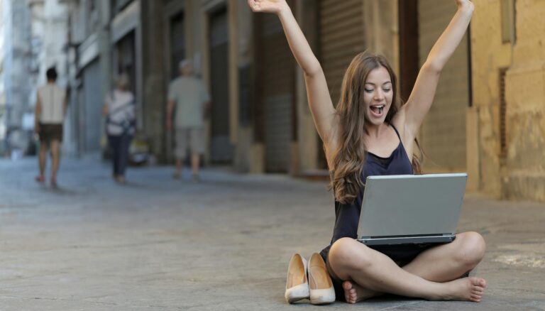 woman raising her hands up while sitting on floor with macbook pro on lap