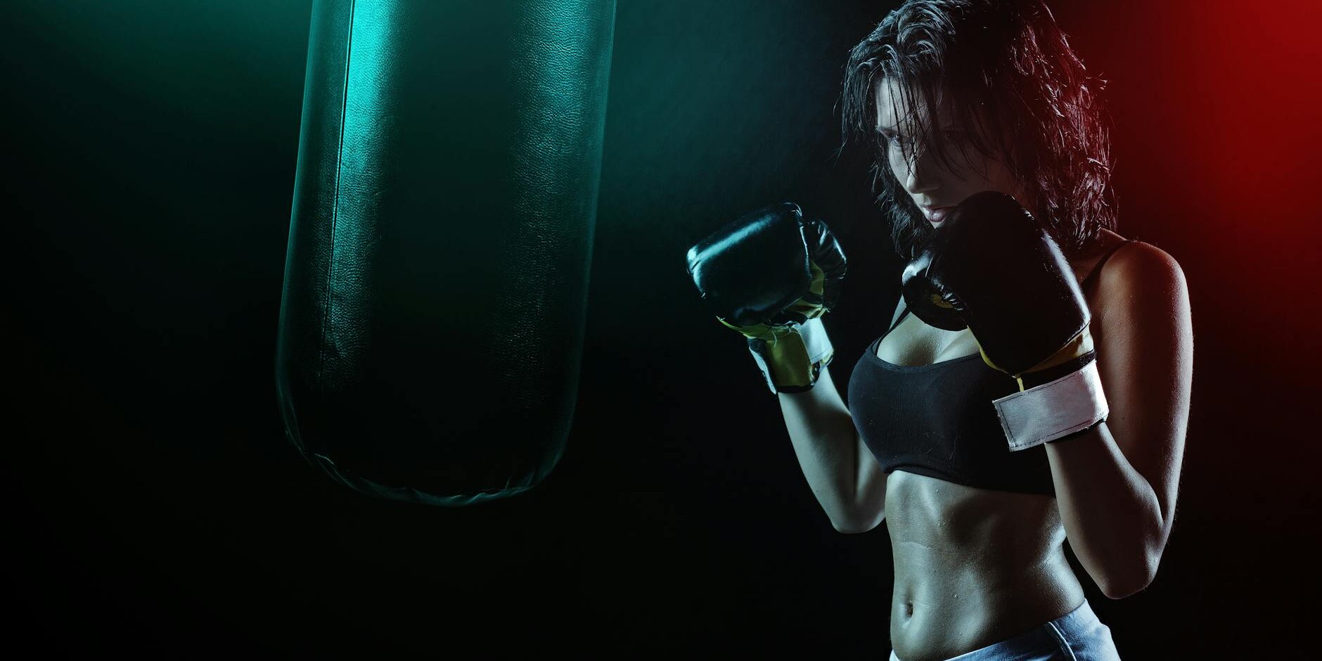 woman in boxing gloves with sports bra posing boxing style in front of punching bag