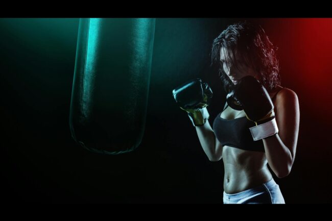 woman in boxing gloves with sports bra posing boxing style in front of punching bag