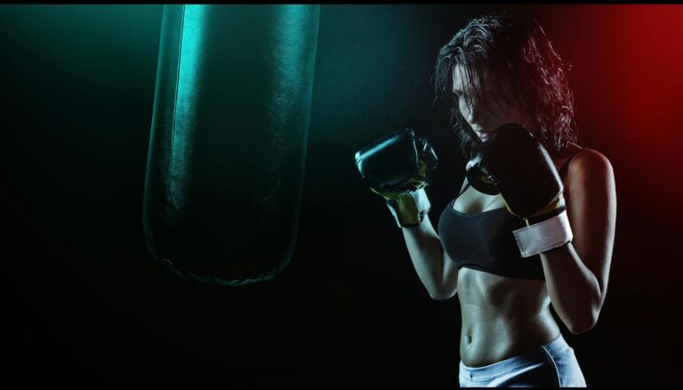 woman in boxing gloves with sports bra posing boxing style in front of punching bag