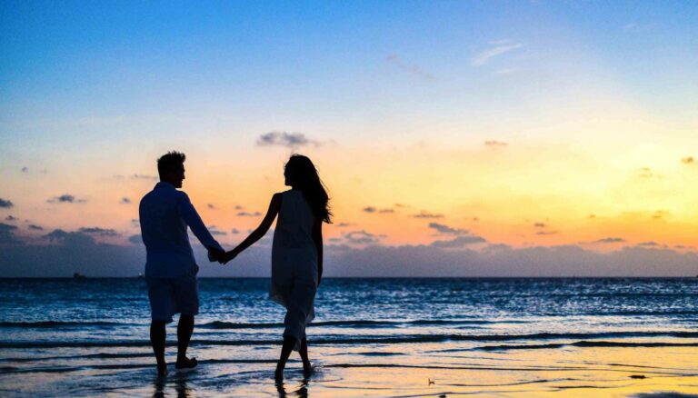 man and woman holding hands walking on seashore during sunrise