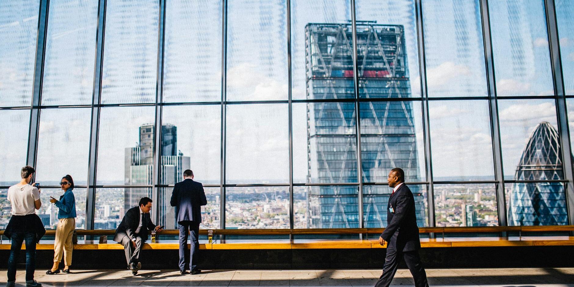 man walking on sidewalk near people standing and sitting beside curtain wall building