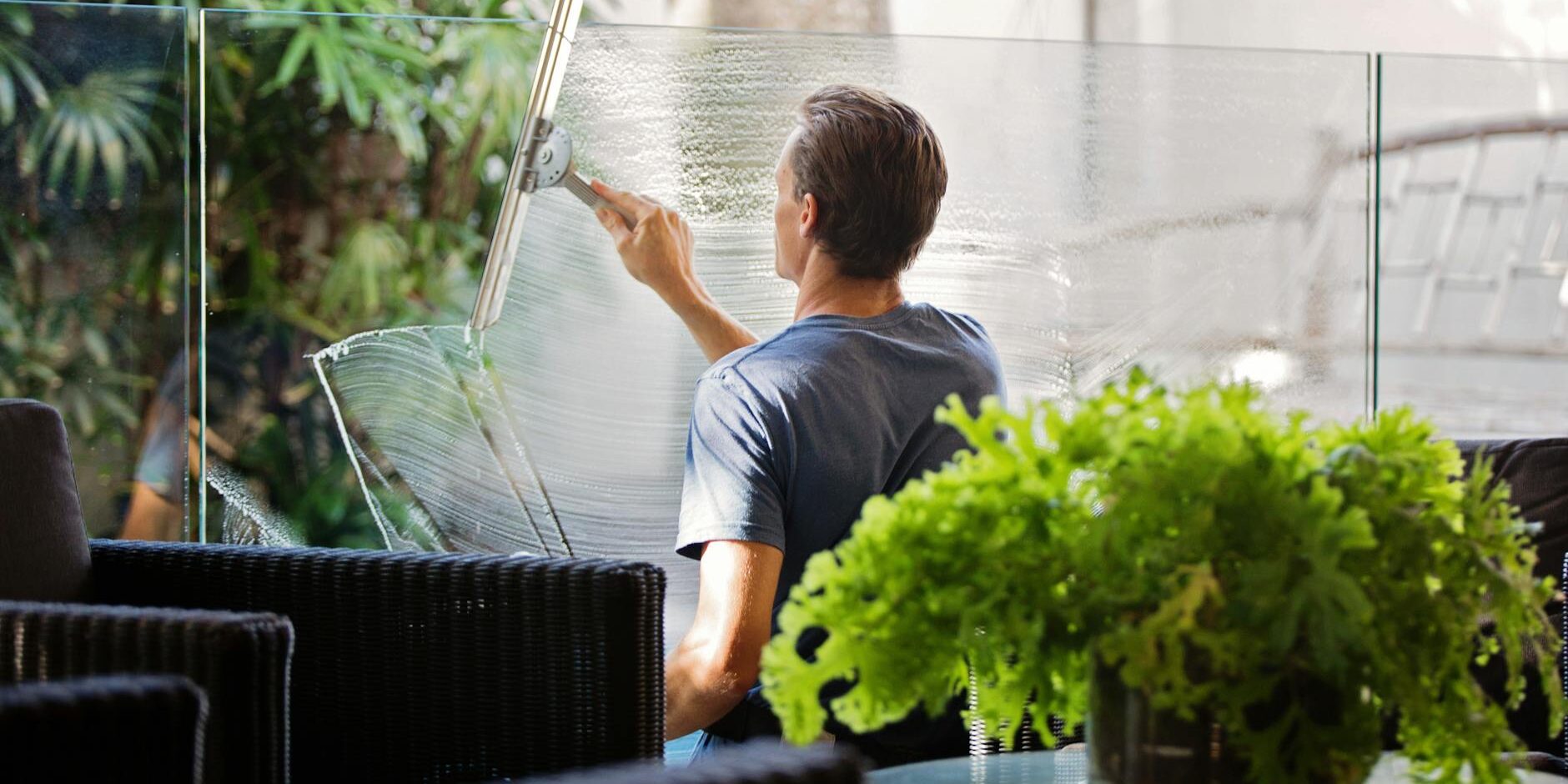 man in gray shirt cleaning clear glass wall near sofa