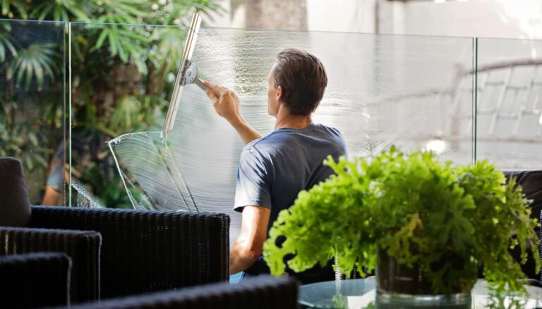 man in gray shirt cleaning clear glass wall near sofa