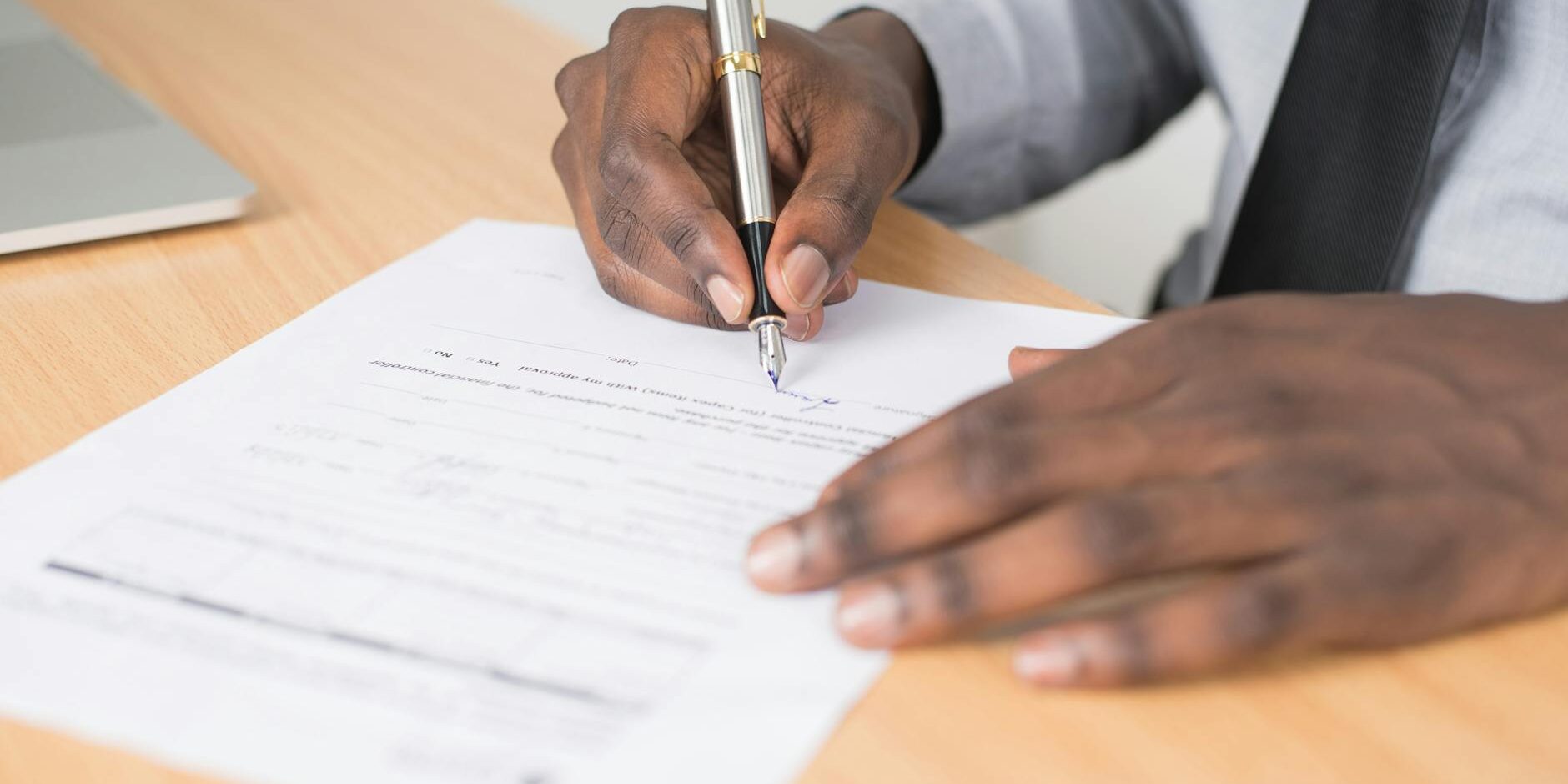 person holding gray twist pen and white printer paper on brown wooden table