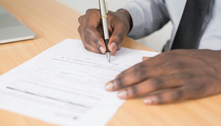 person holding gray twist pen and white printer paper on brown wooden table