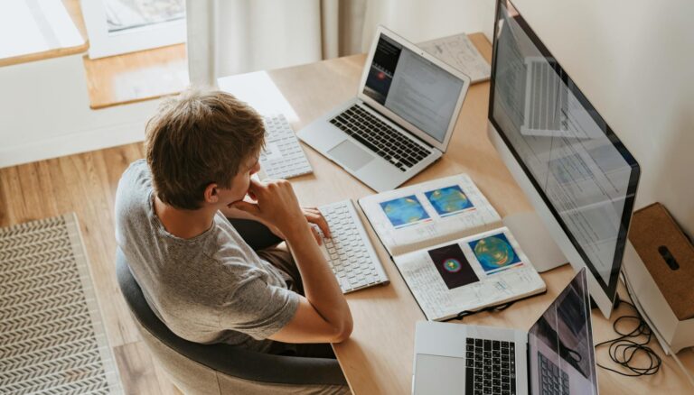 high angle shot of a boy sitting on grey chair while using his laptop computers
