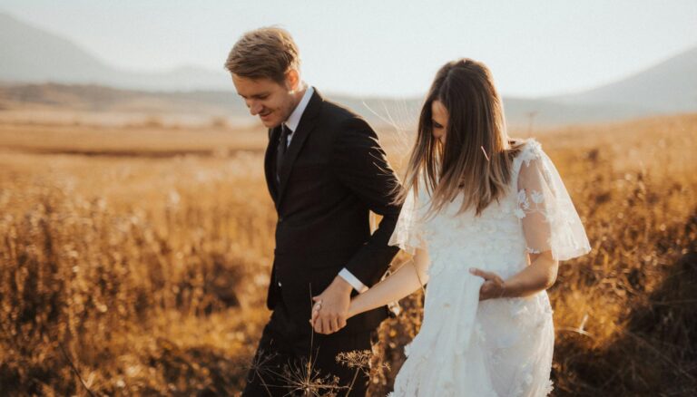 shallow focus photo of man in black formal suit holding woman s hand in white dress
