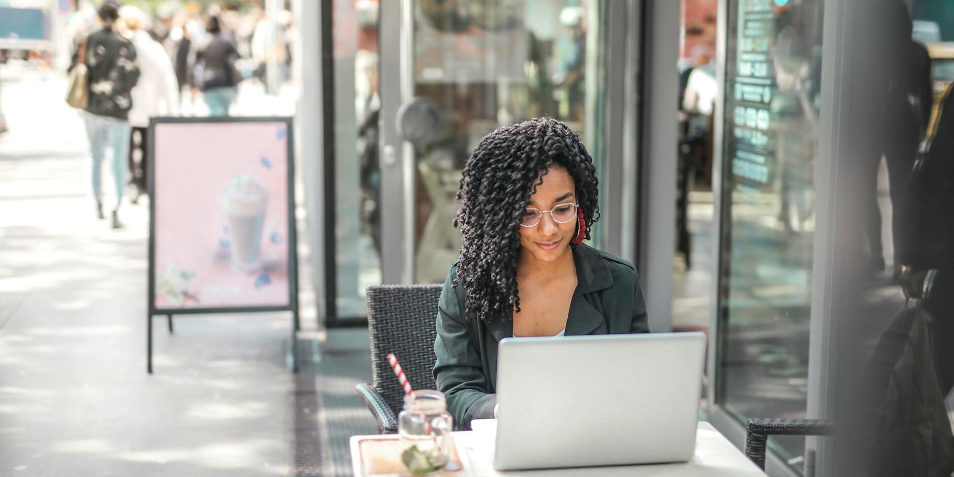 ethnic young woman using laptop while having tasty beverage in modern street cafe