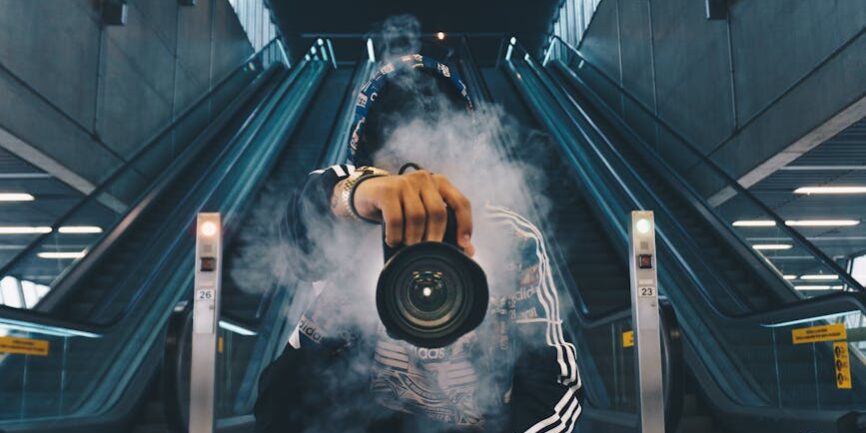 man holding camera while squating with smoke on face inside building