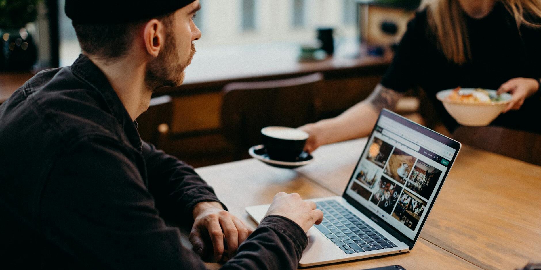 man wearing black jacket using laptop computer sitting beside table