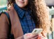 woman in trendy coat and checkered shirt using smartphone