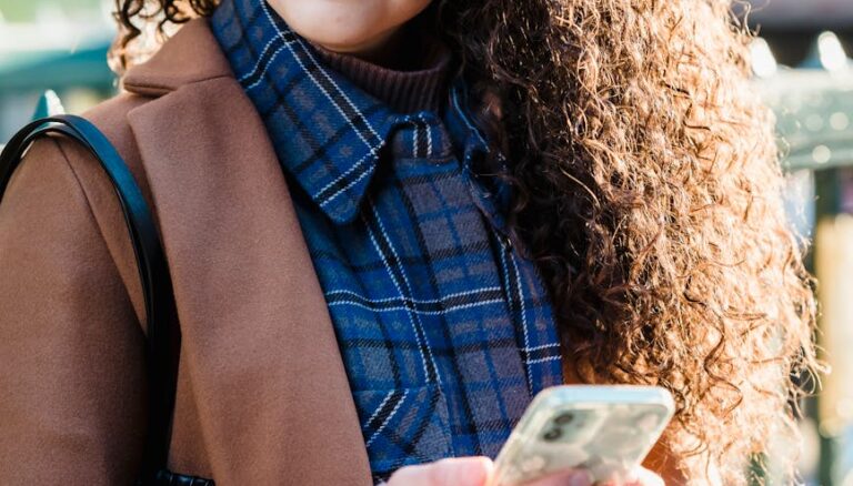 woman in trendy coat and checkered shirt using smartphone