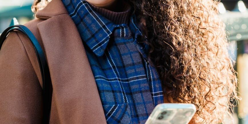 woman in trendy coat and checkered shirt using smartphone
