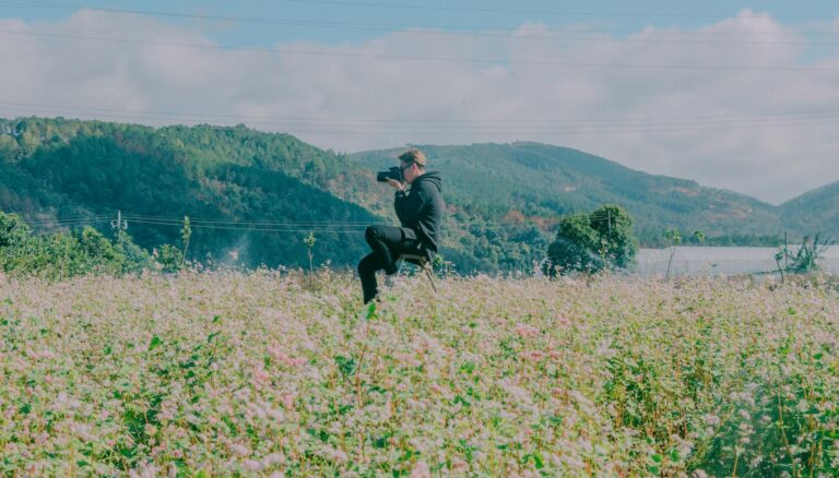 man sitting in the middle of flower field using black dslr camera