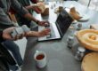 people standing beside man using laptop on gray table with silicon forms