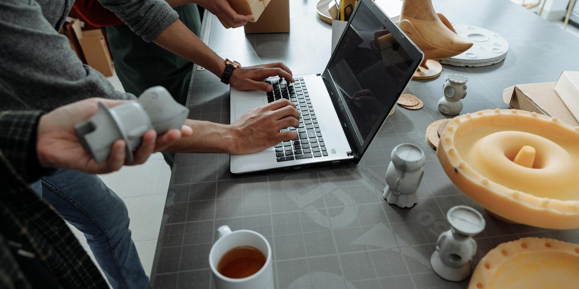 people standing beside man using laptop on gray table with silicon forms