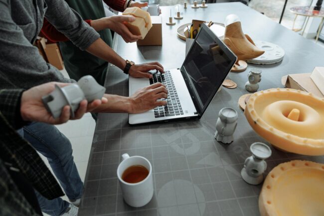 people standing beside man using laptop on gray table with silicon forms