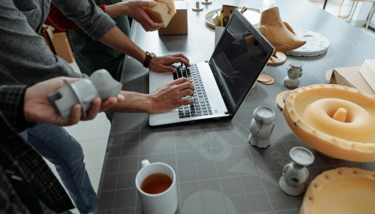 people standing beside man using laptop on gray table with silicon forms