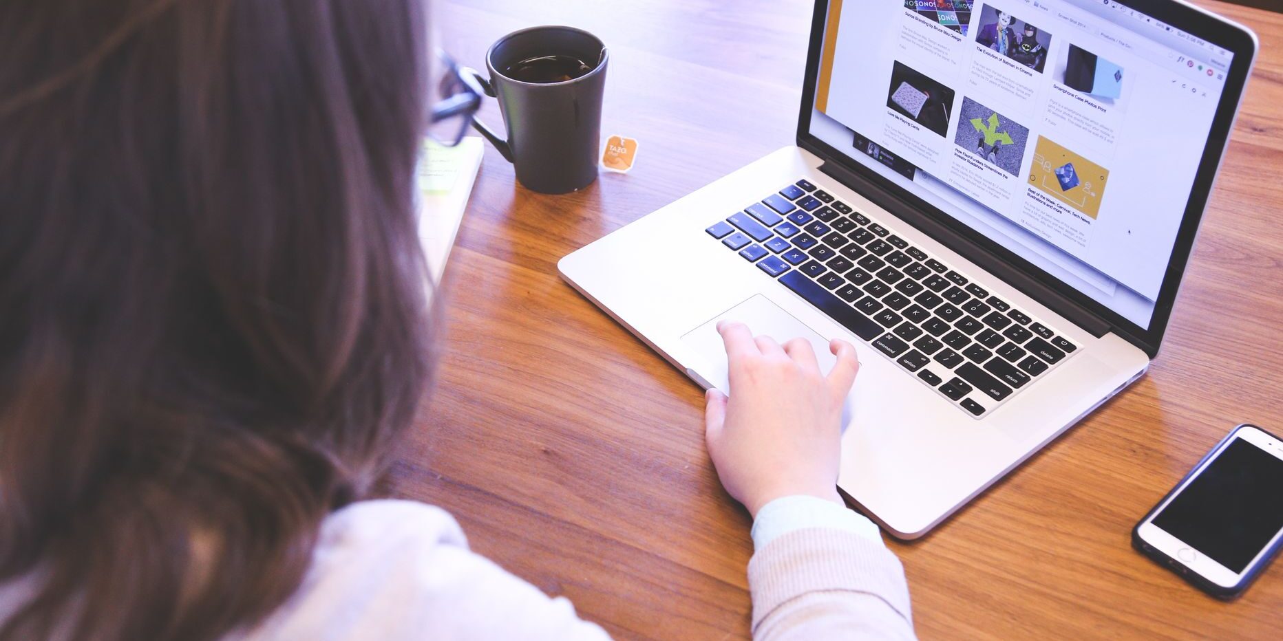 woman swiping touchpad on macbook pro on table near smartphone and mug