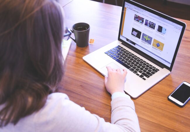 woman swiping touchpad on macbook pro on table near smartphone and mug