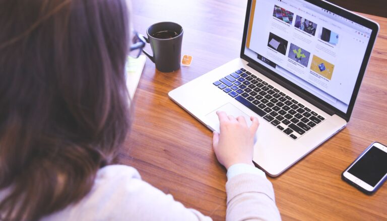 woman swiping touchpad on macbook pro on table near smartphone and mug