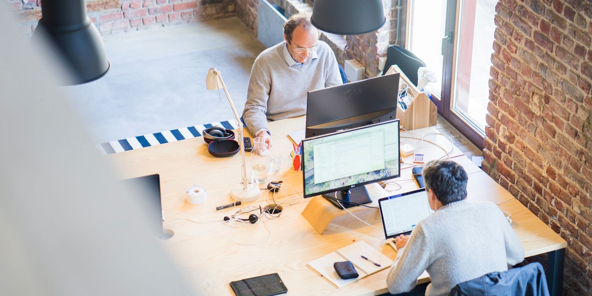 two men sitting facing on flat screen monitors