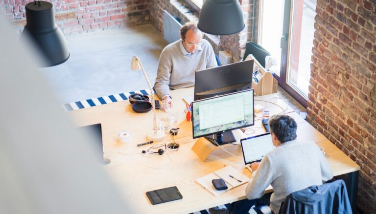 two men sitting facing on flat screen monitors