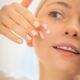 woman applying moisturizer to face close up