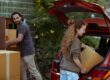couple getting carton boxes out of red car while relocating in new home