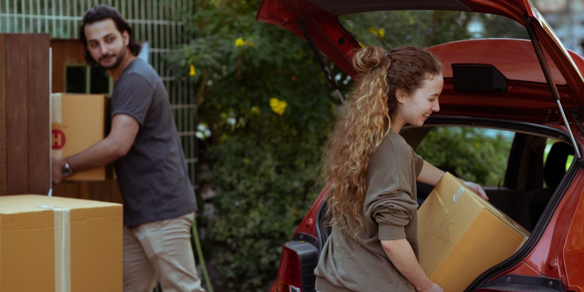 couple getting carton boxes out of red car while relocating in new home