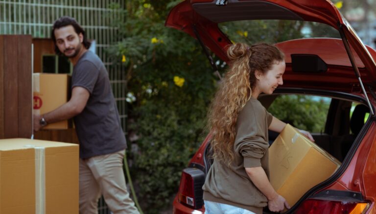 couple getting carton boxes out of red car while relocating in new home