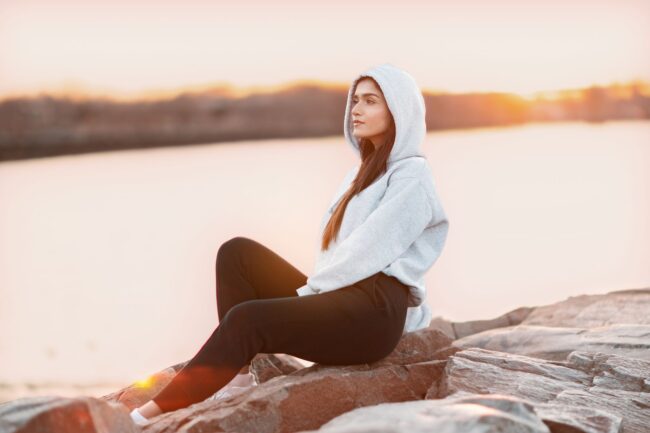 woman in gray hoodie sitting on rock
