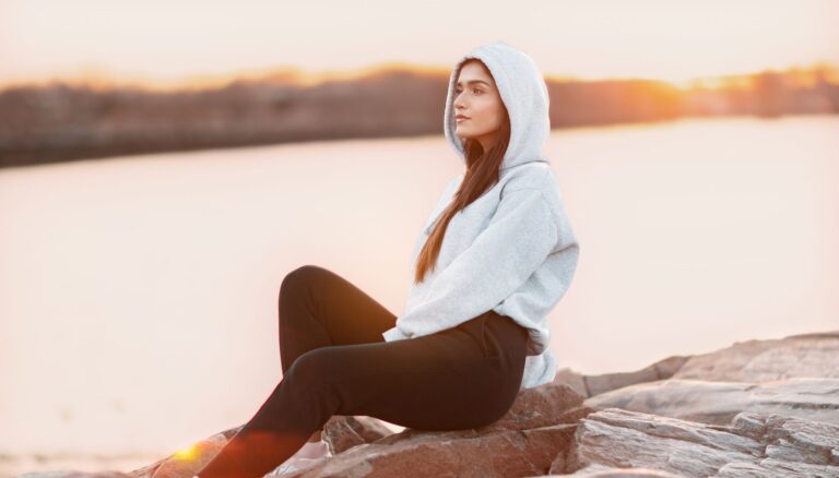 woman in gray hoodie sitting on rock